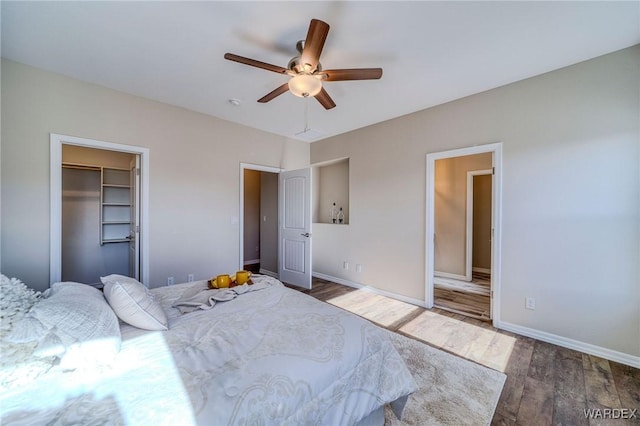 bedroom with ceiling fan, a spacious closet, dark wood-style flooring, and baseboards