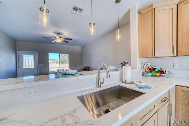 kitchen with light stone counters, decorative light fixtures, visible vents, light brown cabinetry, and a sink