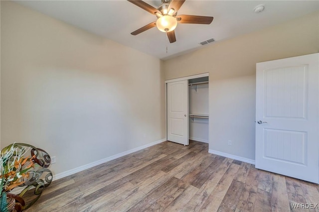 unfurnished bedroom with a closet, visible vents, baseboards, and wood finished floors