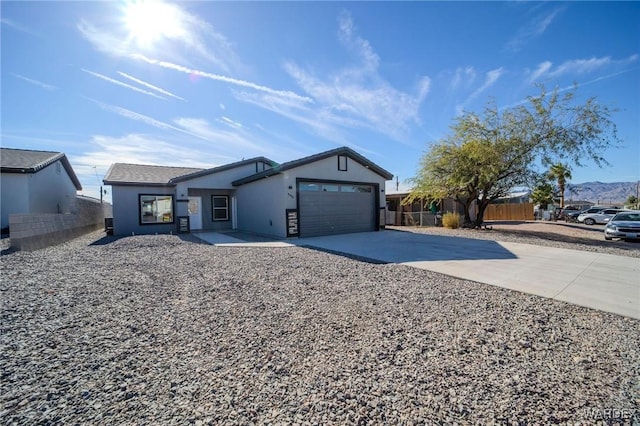 ranch-style home with concrete driveway, fence, an attached garage, and stucco siding