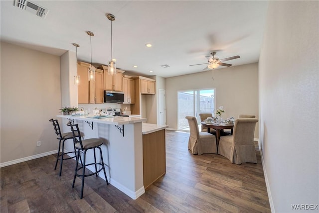 kitchen featuring a peninsula, a kitchen breakfast bar, light countertops, hanging light fixtures, and stainless steel microwave