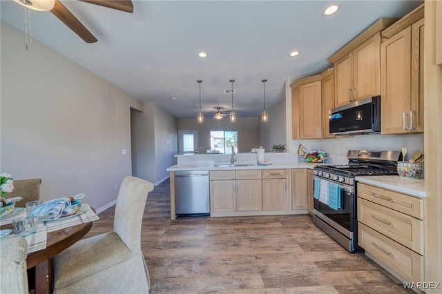 kitchen featuring stainless steel appliances, a peninsula, light countertops, light brown cabinetry, and decorative light fixtures