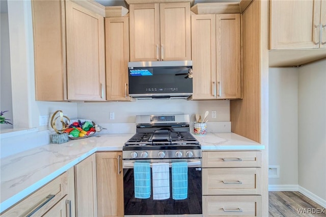 kitchen with light stone countertops, stainless steel gas range oven, and light brown cabinetry