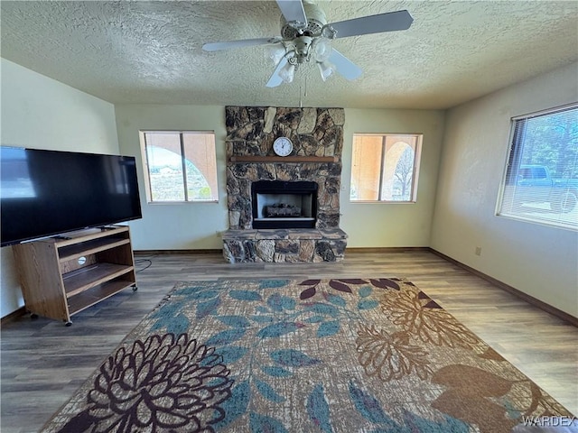 living area featuring a textured ceiling, ceiling fan, a fireplace, and wood finished floors