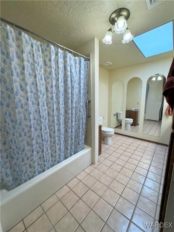 full bath featuring a textured ceiling, shower / bath combo with shower curtain, tile patterned flooring, and toilet