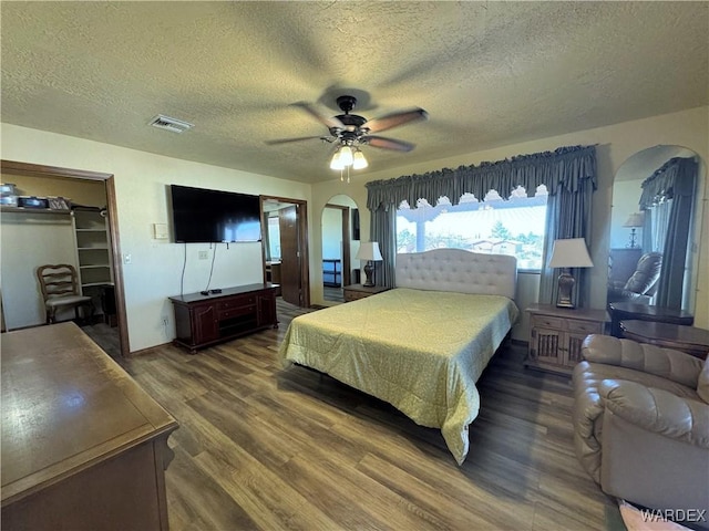 bedroom with arched walkways, visible vents, ceiling fan, a textured ceiling, and wood finished floors