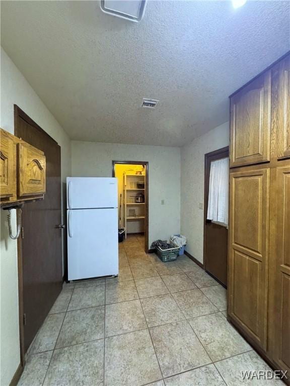 kitchen with light tile patterned floors, a textured ceiling, visible vents, freestanding refrigerator, and brown cabinetry