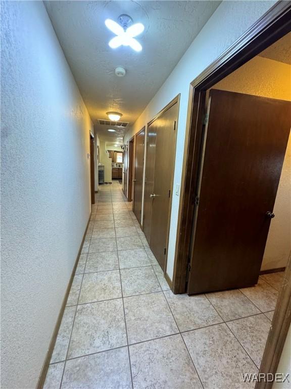 corridor with light tile patterned flooring, a textured wall, and a textured ceiling