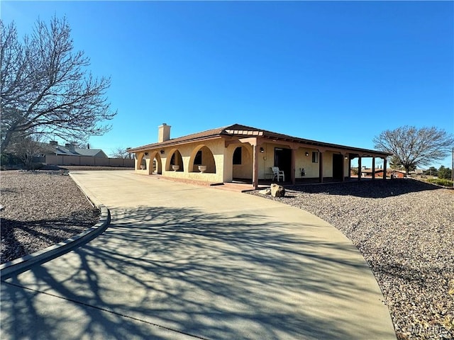 mediterranean / spanish-style house with concrete driveway, fence, a chimney, and stucco siding