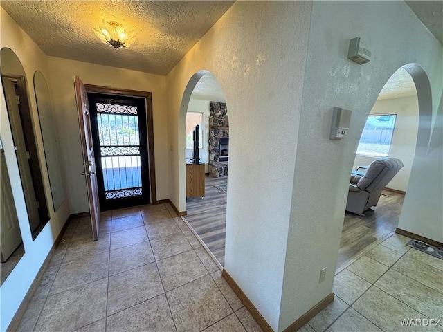 foyer entrance featuring arched walkways, a textured wall, a textured ceiling, and light tile patterned floors