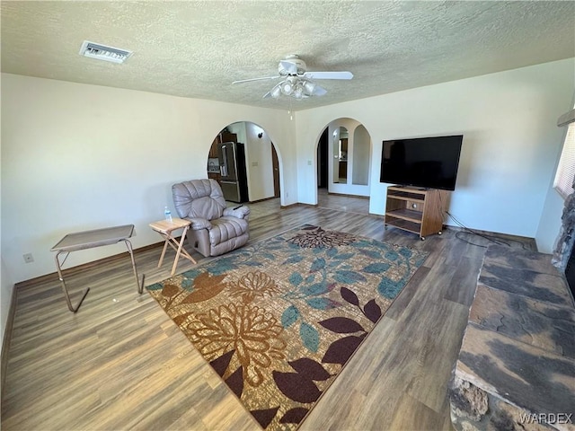 living room with visible vents, a textured ceiling, arched walkways, and wood finished floors