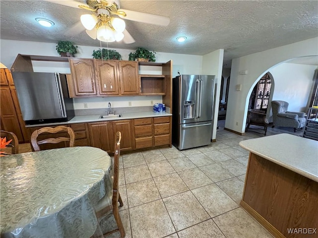 kitchen with arched walkways, brown cabinets, open shelves, a sink, and high end refrigerator