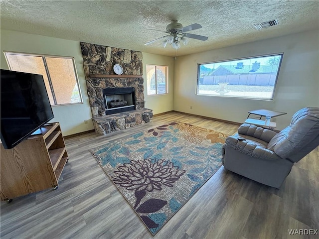 living area with a textured ceiling, a fireplace, wood finished floors, and visible vents