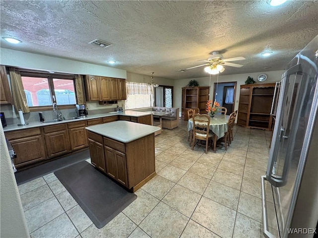 kitchen with ceiling fan, a center island, light countertops, a sink, and light tile patterned flooring