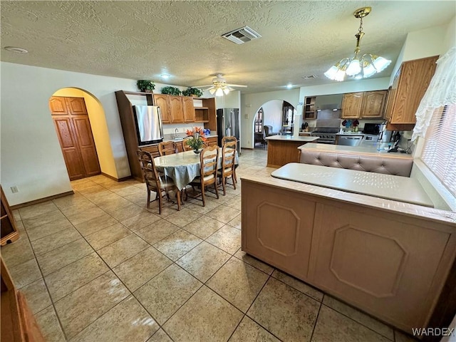 kitchen featuring arched walkways, under cabinet range hood, a peninsula, stainless steel appliances, and visible vents