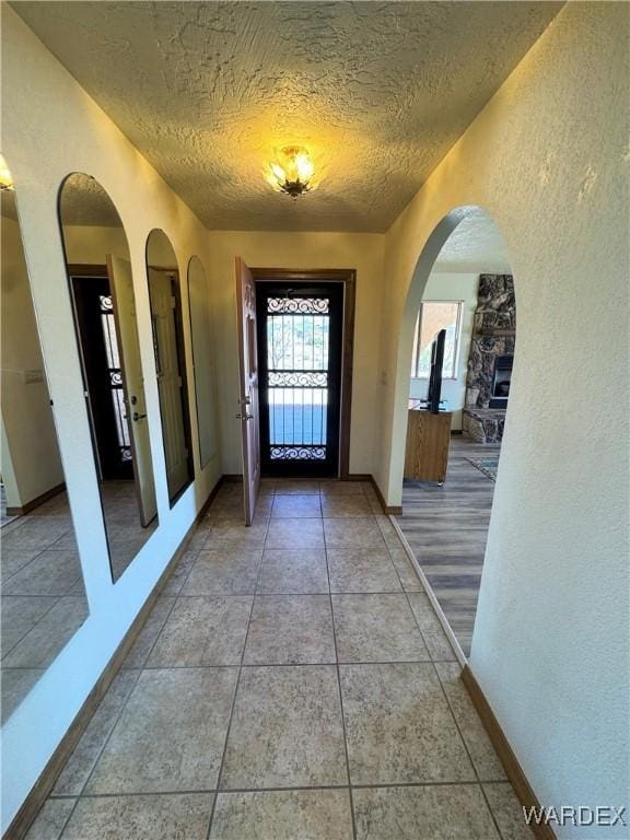 entrance foyer featuring light tile patterned floors, baseboards, arched walkways, a textured wall, and a textured ceiling