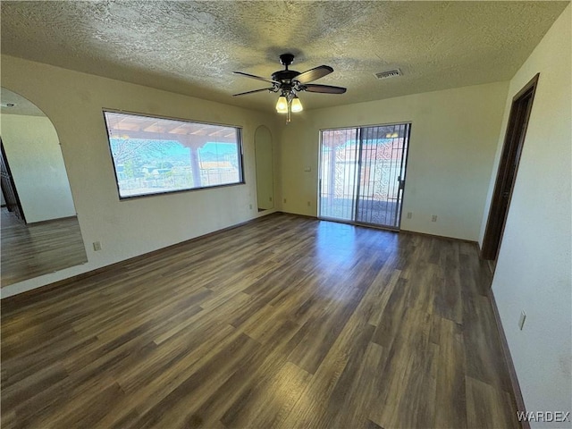 spare room featuring arched walkways, a healthy amount of sunlight, visible vents, and wood finished floors