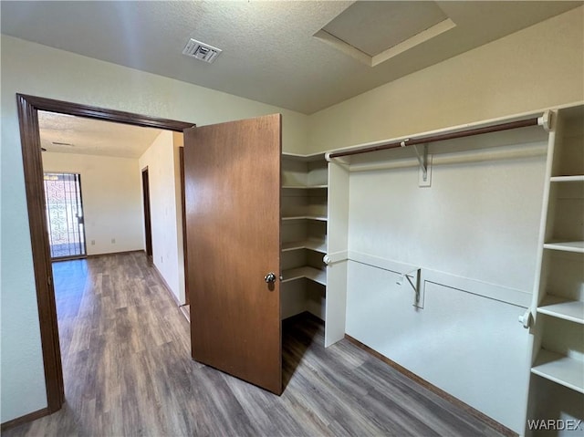 walk in closet with wood finished floors, visible vents, and attic access