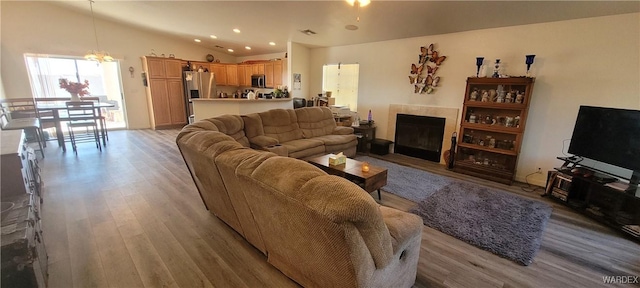 living room with lofted ceiling, light wood-style flooring, a fireplace, a chandelier, and recessed lighting