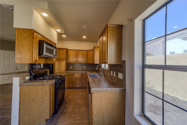 2230 Diamond Creek Rd, Bullhead City, AZ 86442 - kitchen featuring black range with gas stovetop, stainless steel microwave, backsplash, brown cabinetry, and dark tile patterned floors