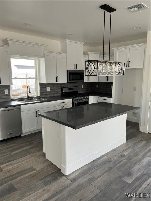 kitchen with appliances with stainless steel finishes, dark countertops, a kitchen island, and pendant lighting