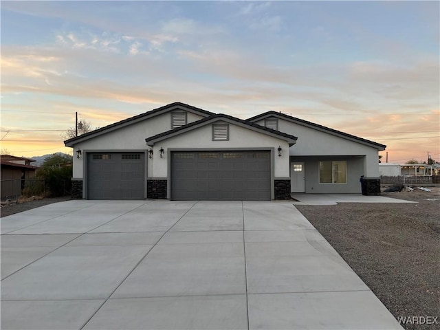 view of front of property featuring concrete driveway, stone siding, an attached garage, and stucco siding