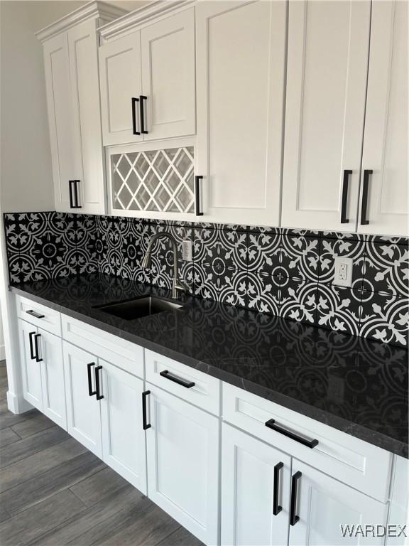 kitchen featuring dark wood finished floors, decorative backsplash, dark stone counters, white cabinetry, and a sink