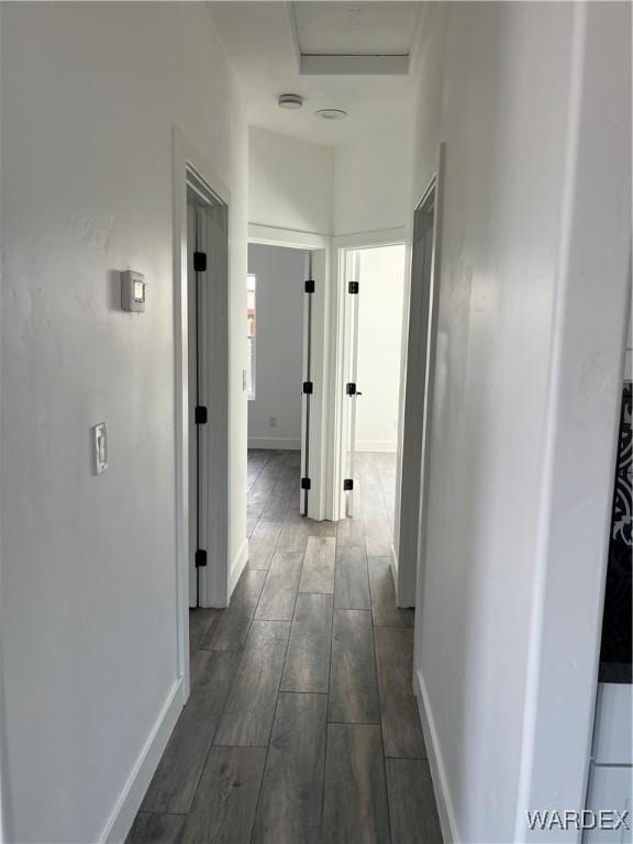 corridor featuring attic access, wood tiled floor, and baseboards