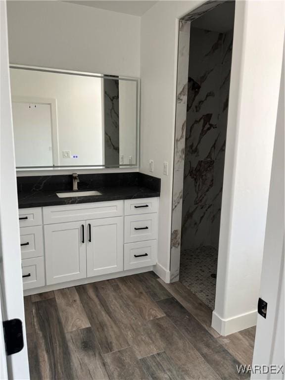 full bath featuring a marble finish shower, wood finished floors, vanity, and baseboards