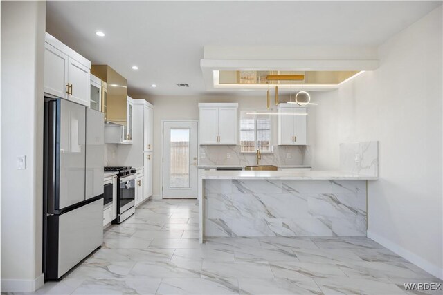 kitchen featuring glass insert cabinets, freestanding refrigerator, hanging light fixtures, white cabinetry, and stainless steel range with gas stovetop