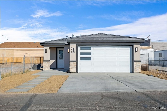 prairie-style house featuring stone siding, concrete driveway, fence, and stucco siding