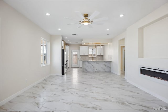 unfurnished living room with marble finish floor, recessed lighting, a glass covered fireplace, ceiling fan, and baseboards