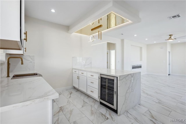 kitchen with beverage cooler, visible vents, white cabinets, open floor plan, and a sink