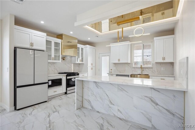 kitchen featuring glass insert cabinets, freestanding refrigerator, white cabinets, stainless steel gas stove, and light stone countertops