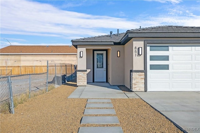 doorway to property featuring an attached garage, fence, stone siding, driveway, and stucco siding