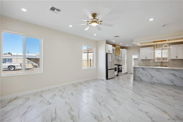 kitchen with stainless steel gas stove, visible vents, decorative backsplash, freestanding refrigerator, and white cabinetry