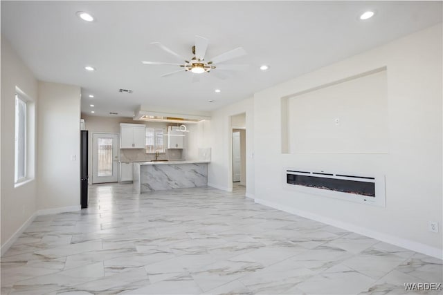 unfurnished living room with marble finish floor, recessed lighting, visible vents, a glass covered fireplace, and baseboards