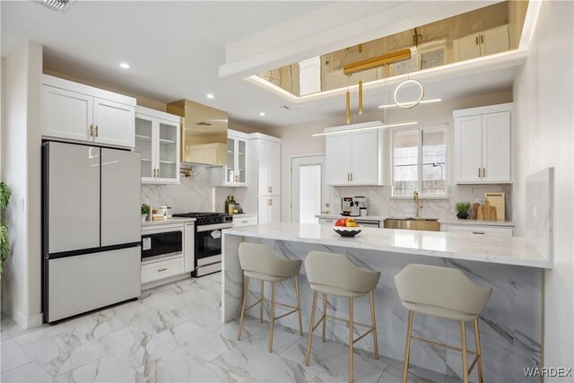 kitchen with light stone counters, glass insert cabinets, refrigerator, white cabinetry, and stainless steel range with gas stovetop