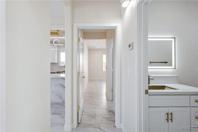 hall with marble finish floor, a sink, and baseboards