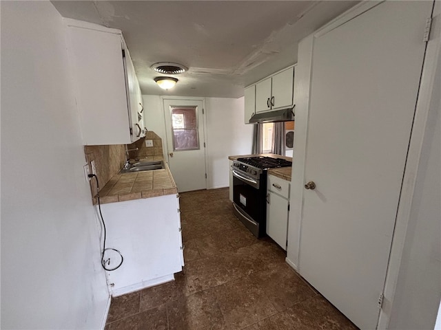 kitchen with a sink, stainless steel gas stove, tile countertops, under cabinet range hood, and white cabinetry