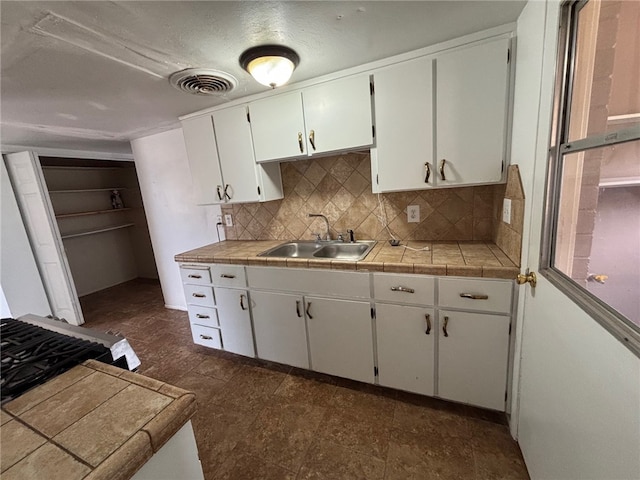 kitchen with a sink, tile counters, white cabinetry, visible vents, and tasteful backsplash