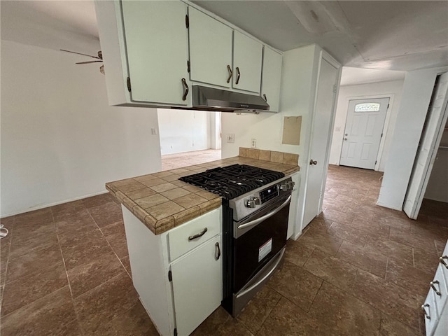 kitchen with under cabinet range hood, stainless steel gas range oven, tile counters, and stone finish flooring