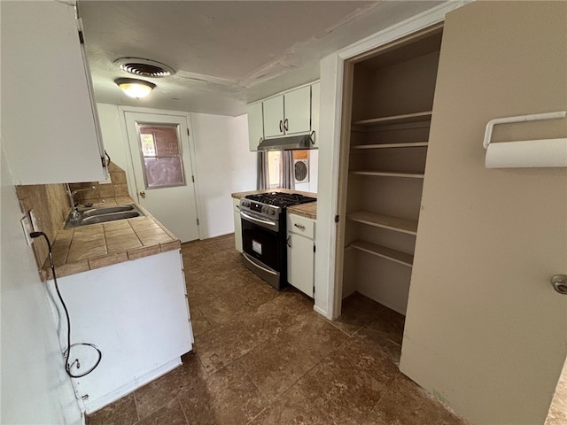 kitchen featuring a sink, tile countertops, under cabinet range hood, white cabinets, and stainless steel gas range