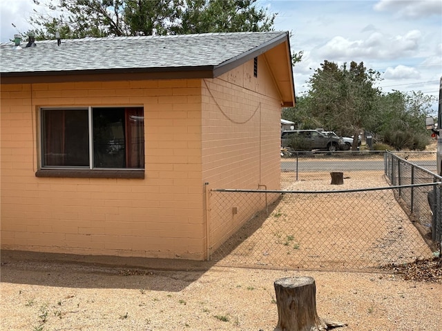 view of home's exterior featuring a shingled roof, fence, and concrete block siding