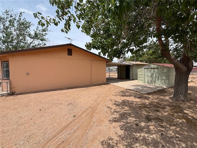 view of side of property with an attached carport, a storage unit, dirt driveway, fence, and an outbuilding
