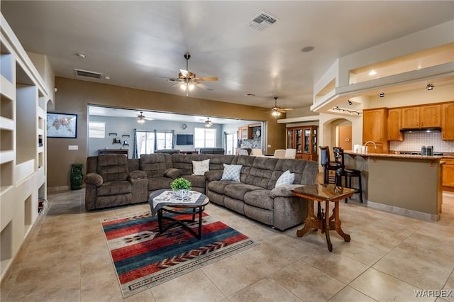 living room featuring light tile patterned floors, ceiling fan, visible vents, and arched walkways