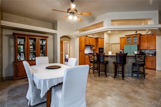 dining area featuring arched walkways, light tile patterned flooring, and a ceiling fan