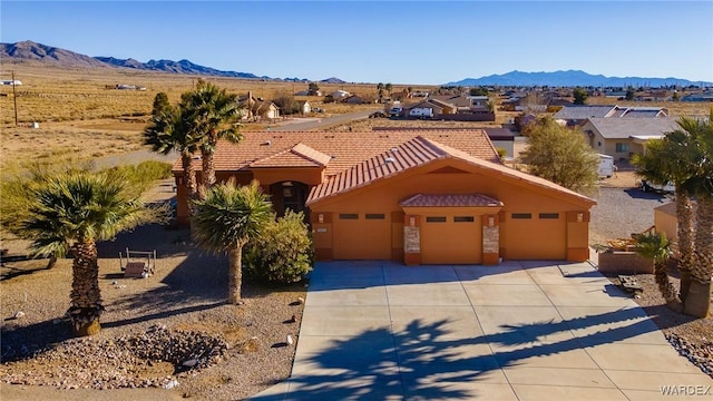 mediterranean / spanish-style home featuring an attached garage, a mountain view, a tile roof, driveway, and stucco siding