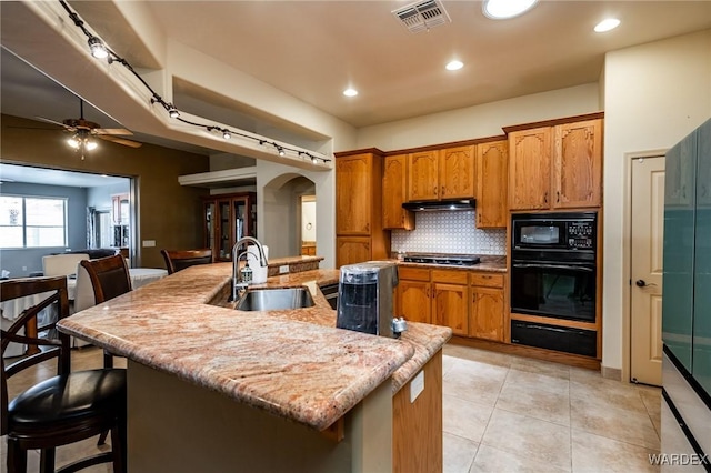 kitchen with visible vents, arched walkways, under cabinet range hood, black appliances, and a warming drawer