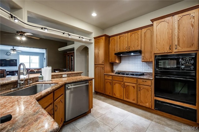 kitchen featuring arched walkways, brown cabinetry, a sink, under cabinet range hood, and black appliances